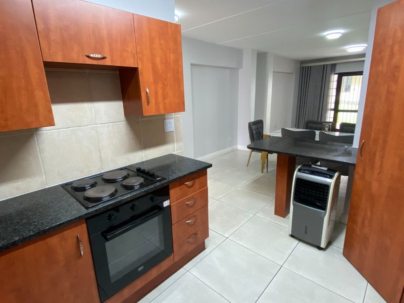 Open-plan kitchen and dining area featuring wood-finish cabinetry, granite countertops, built-in oven and hob, and neutral tiled flooring throughout.