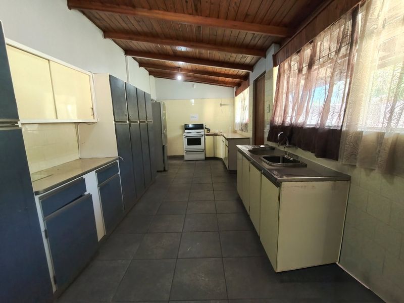 A spacious, dated kitchen featuring dark tiled floors, exposed timber beam ceilings, extensive cabinetry, and a freestanding stove.