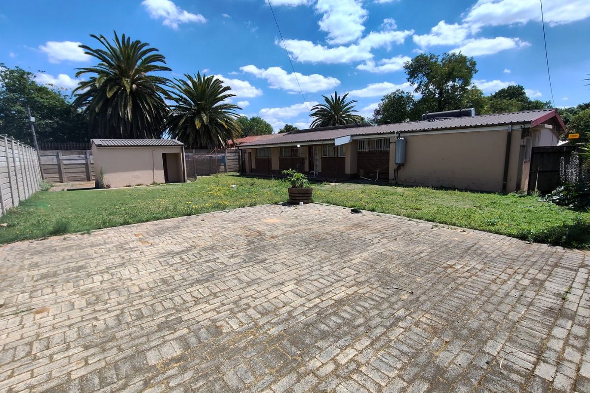 Spacious rear exterior featuring a large paved area, a detached outbuilding, and a lawn, enclosed by precast concrete boundary walls.