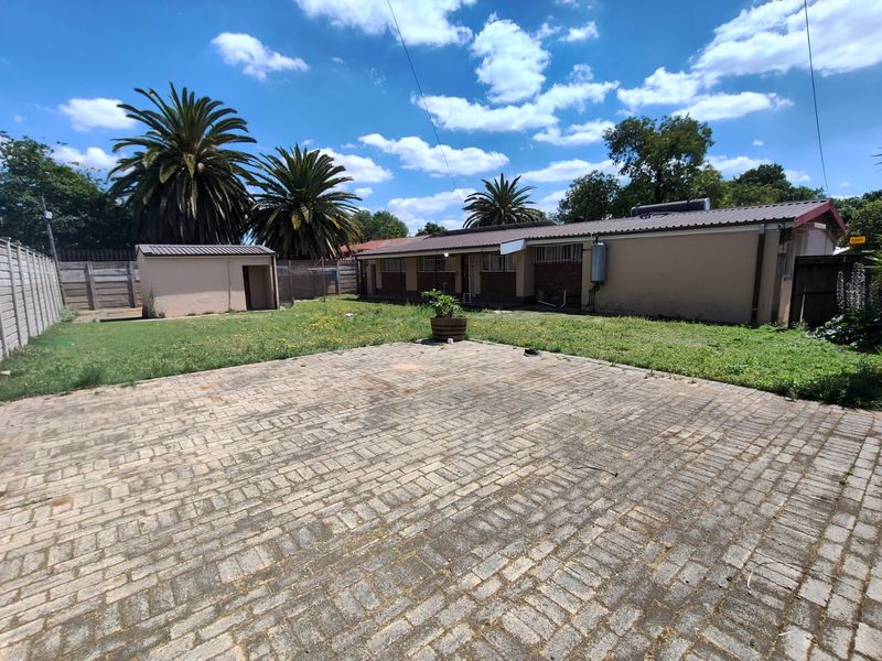 Spacious rear exterior featuring a large paved area, a detached outbuilding, and a lawn, enclosed by precast concrete boundary walls.