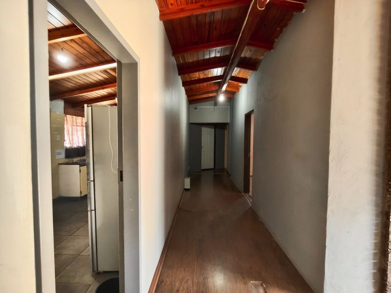 A long hallway featuring exposed timber ceilings and laminate flooring, providing access to adjacent rooms including the kitchen area.