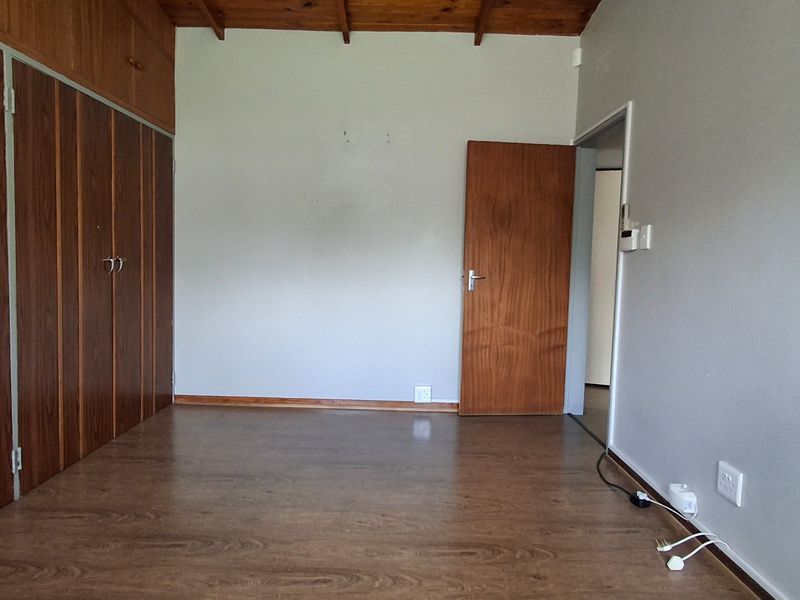 An empty bedroom featuring laminate flooring, exposed timber ceiling beams, and extensive built-in wooden cabinetry.