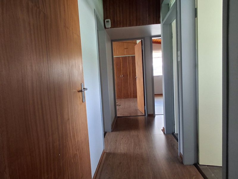 A functional hallway featuring timber veneer doors, laminate flooring, and wood-paneled ceiling details, providing access to adjacent rooms with built-in storage.
