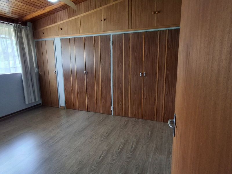 A spacious bedroom featuring extensive built-in wooden cabinetry, a warm timber-paneled ceiling, and modern laminate flooring.