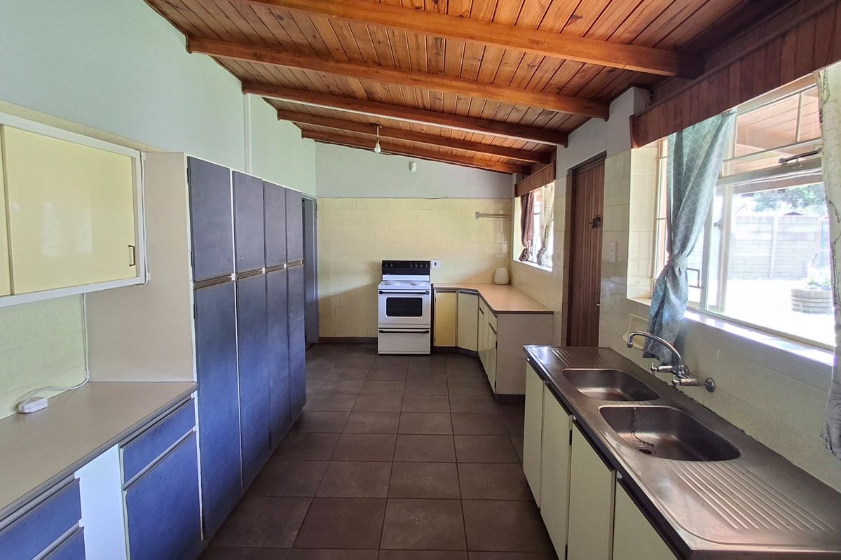 Spacious kitchen featuring built-in cabinetry, a double basin sink, freestanding stove, tiled flooring, and an exposed timber beam ceiling.