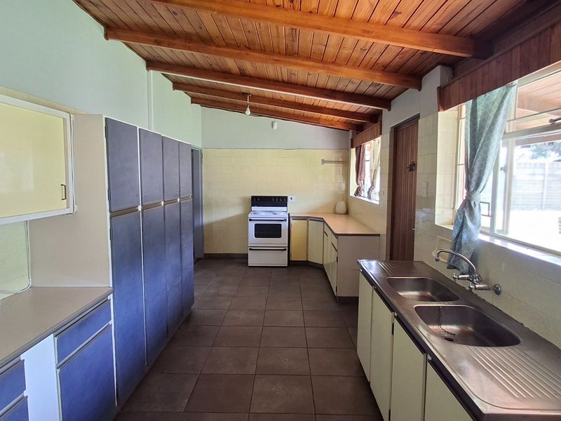 Spacious kitchen featuring built-in cabinetry, a double basin sink, freestanding stove, tiled flooring, and an exposed timber beam ceiling.