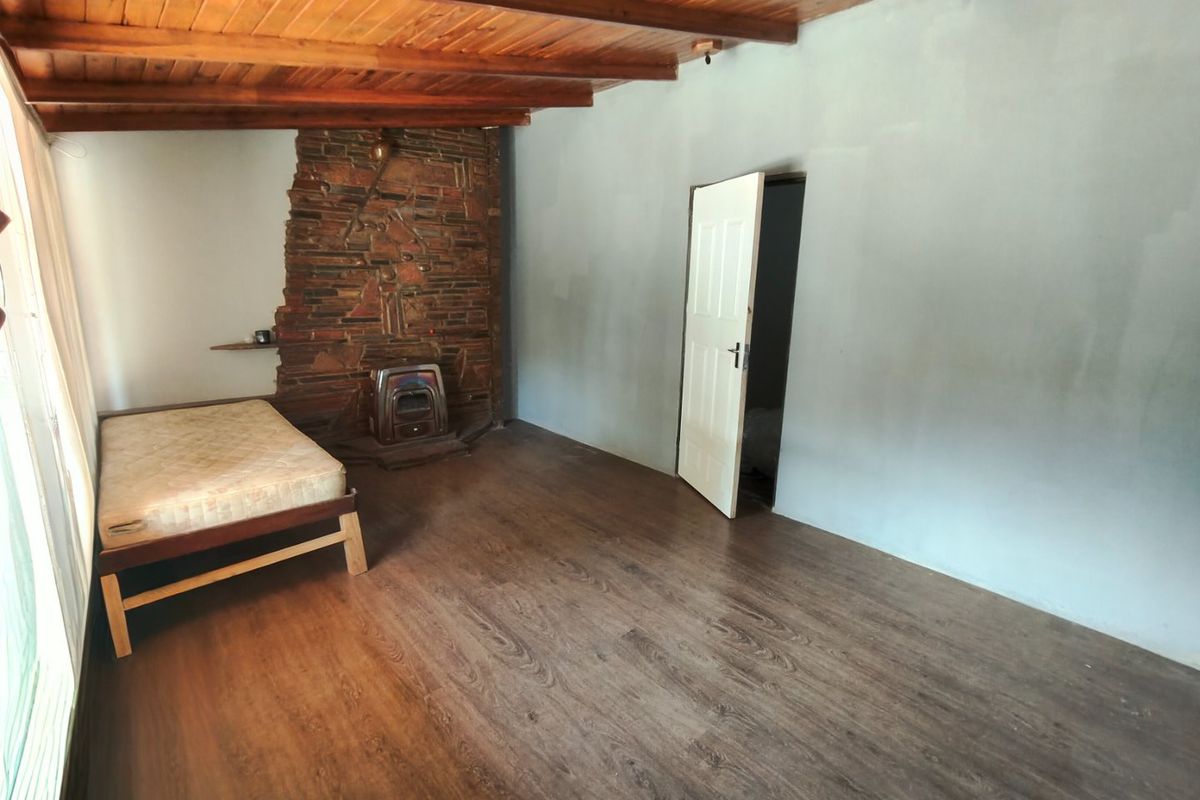 A spacious bedroom featuring exposed timber beam ceilings, a rustic stone fireplace with a built-in stove, and dark laminate flooring.