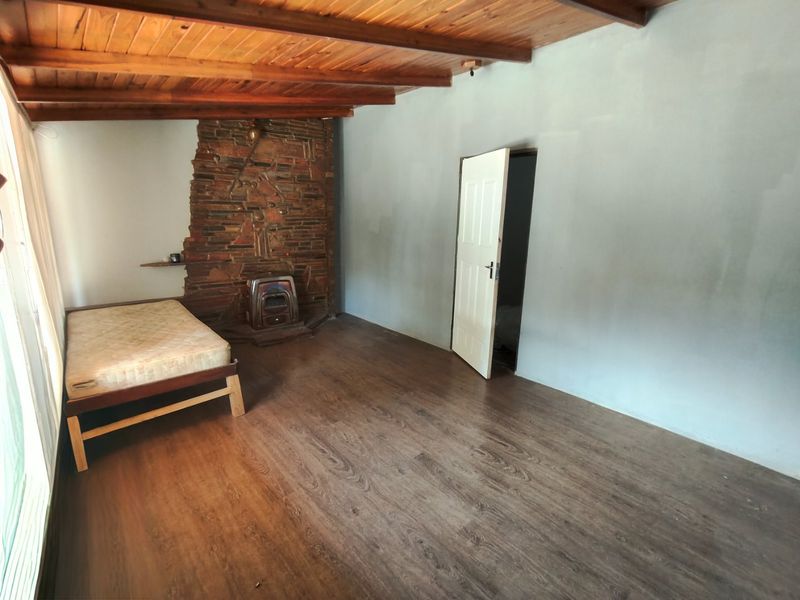 A spacious bedroom featuring exposed timber beam ceilings, a rustic stone fireplace with a built-in stove, and dark laminate flooring.