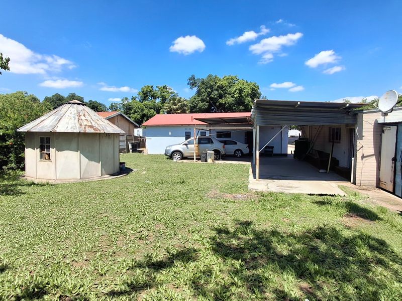 Rear exterior view featuring a large lawn, a detached outbuilding with a metal roof, and a covered carport area attached to the main house.