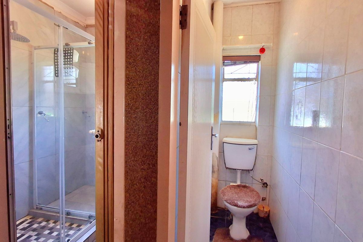 A functional bathroom featuring a separate glass-enclosed shower and a standard toilet, finished with ceramic wall tiling throughout.