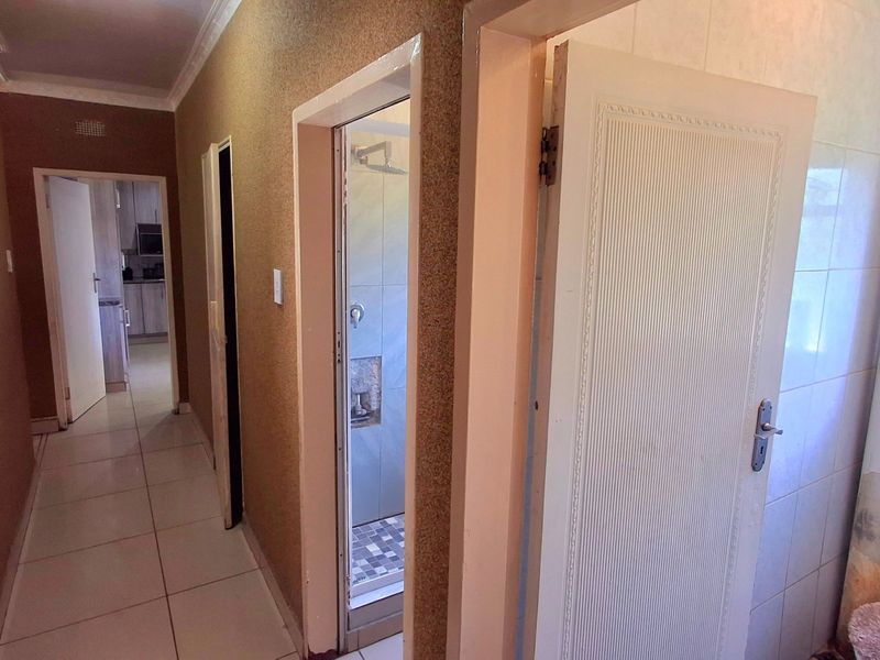 A hallway providing access to a bathroom and kitchen area, featuring tiled flooring and textured wall finishes throughout.