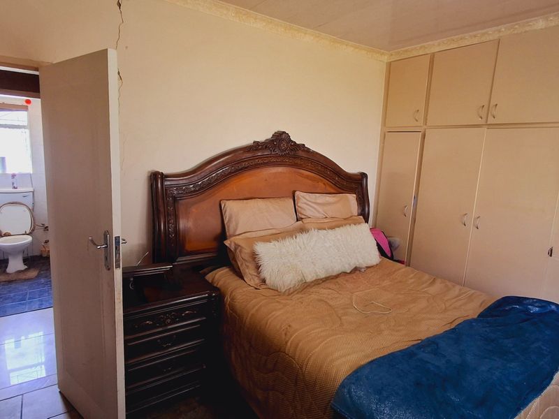 Bedroom featuring built-in cupboards and direct access to an en-suite bathroom, showing visible structural wall cracking.