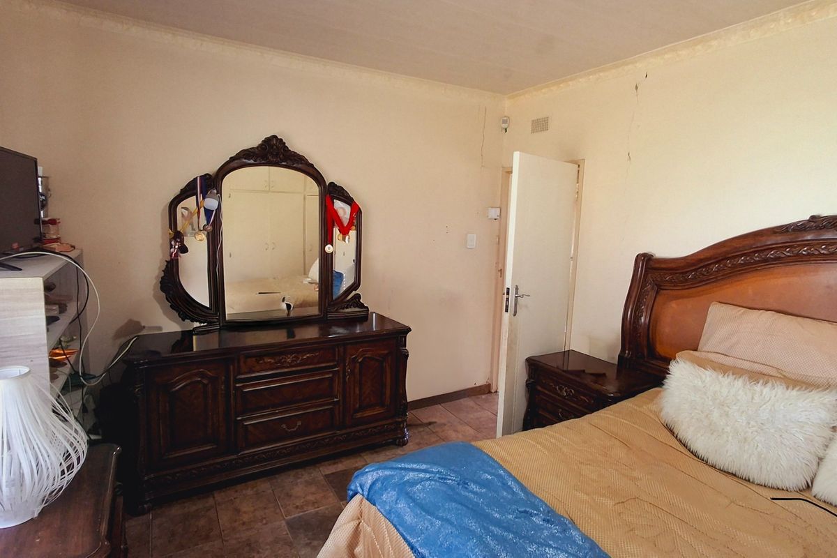 A bedroom featuring tiled flooring and built-in cupboards, showing signs of wear including visible wall cracks.