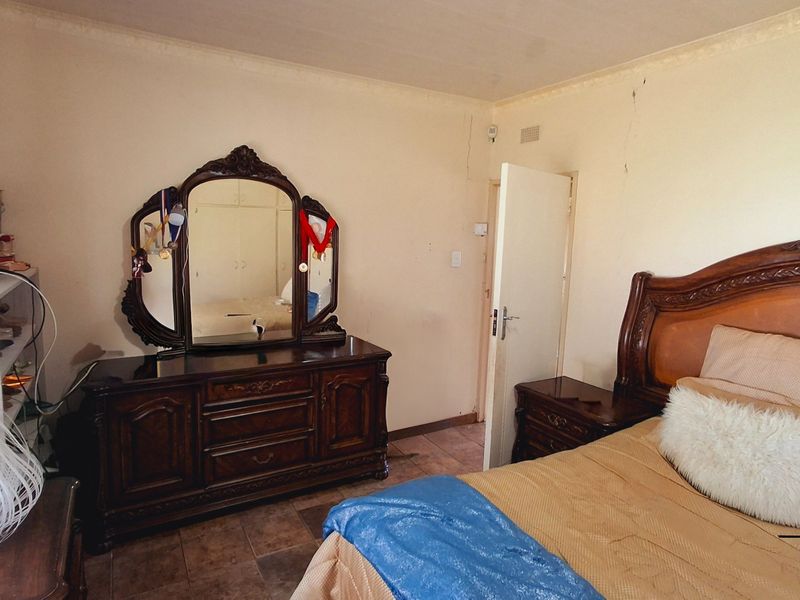 A bedroom featuring tiled flooring and built-in cupboards, showing signs of wear including visible wall cracks.