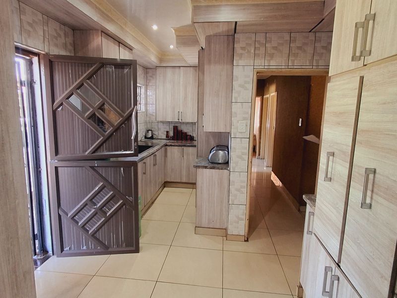 A functional kitchen featuring light wood-finish cabinetry, tiled flooring, and a tiled backsplash, with direct access to an adjacent hallway.
