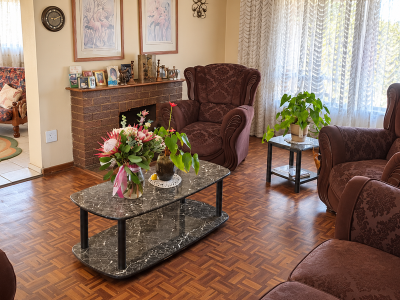 A traditional living room featuring a brick fireplace and classic parquet flooring, offering a warm and inviting atmosphere with natural light.