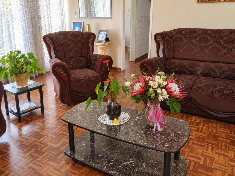 A comfortable living room featuring classic parquet flooring and large windows dressed with sheer curtains, providing a warm and inviting atmosphere.