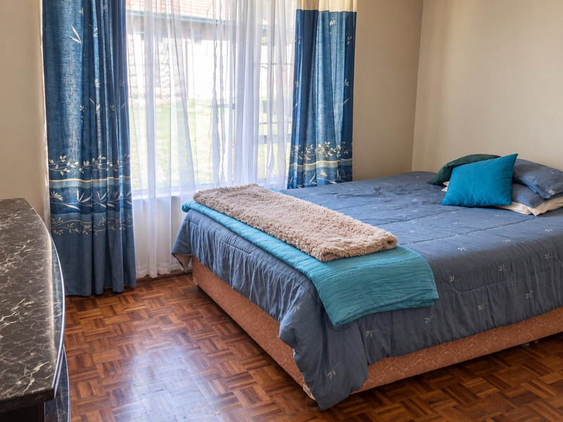A bedroom featuring classic parquet flooring and natural light through a window with curtain rails.