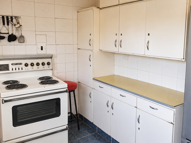A functional kitchen featuring white built-in cabinetry, laminate countertops, tiled backsplash, and a classic freestanding electric stove.