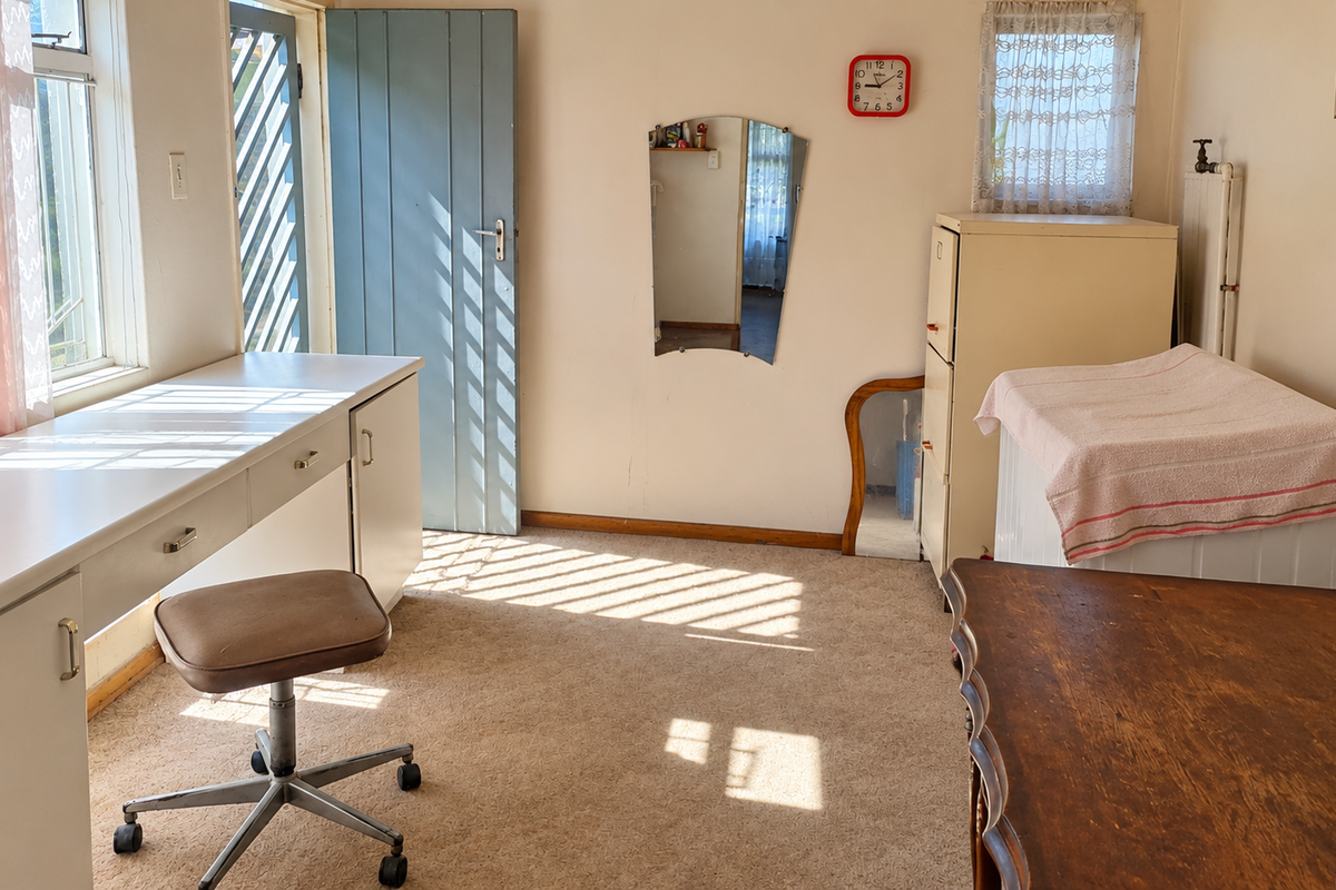 A bedroom featuring a built-in desk, radiator, and natural light from casement windows, offering potential for modernization and refreshed interior finishes.