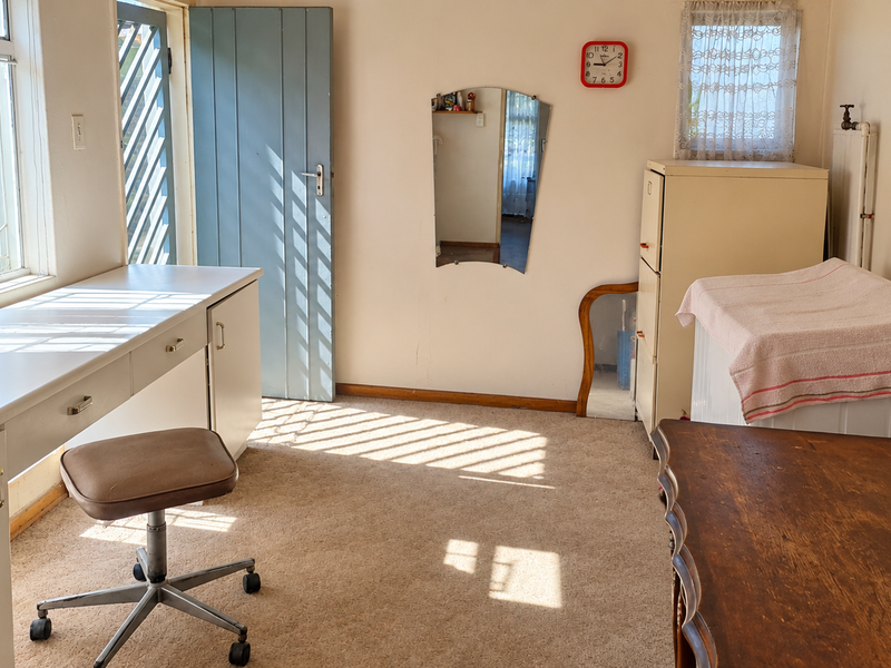 A bedroom featuring a built-in desk, radiator, and natural light from casement windows, offering potential for modernization and refreshed interior finishes.