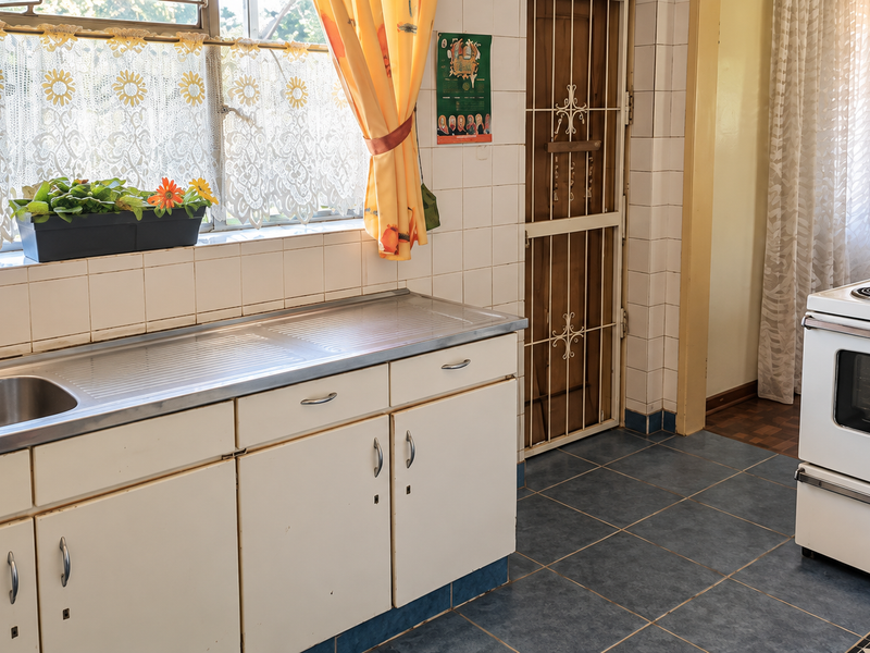 A functional kitchen featuring a stainless steel sink, tiled splashback, built-in cabinetry, and a freestanding electric stove with a security gate entrance.