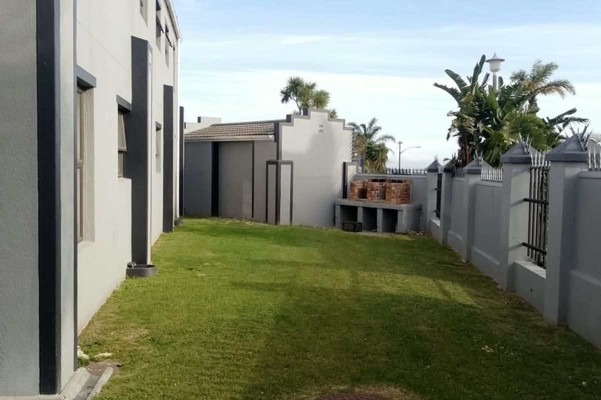 A private rear garden area featuring a built-in brick braai, manicured lawn, and secure perimeter walling with metal fencing.