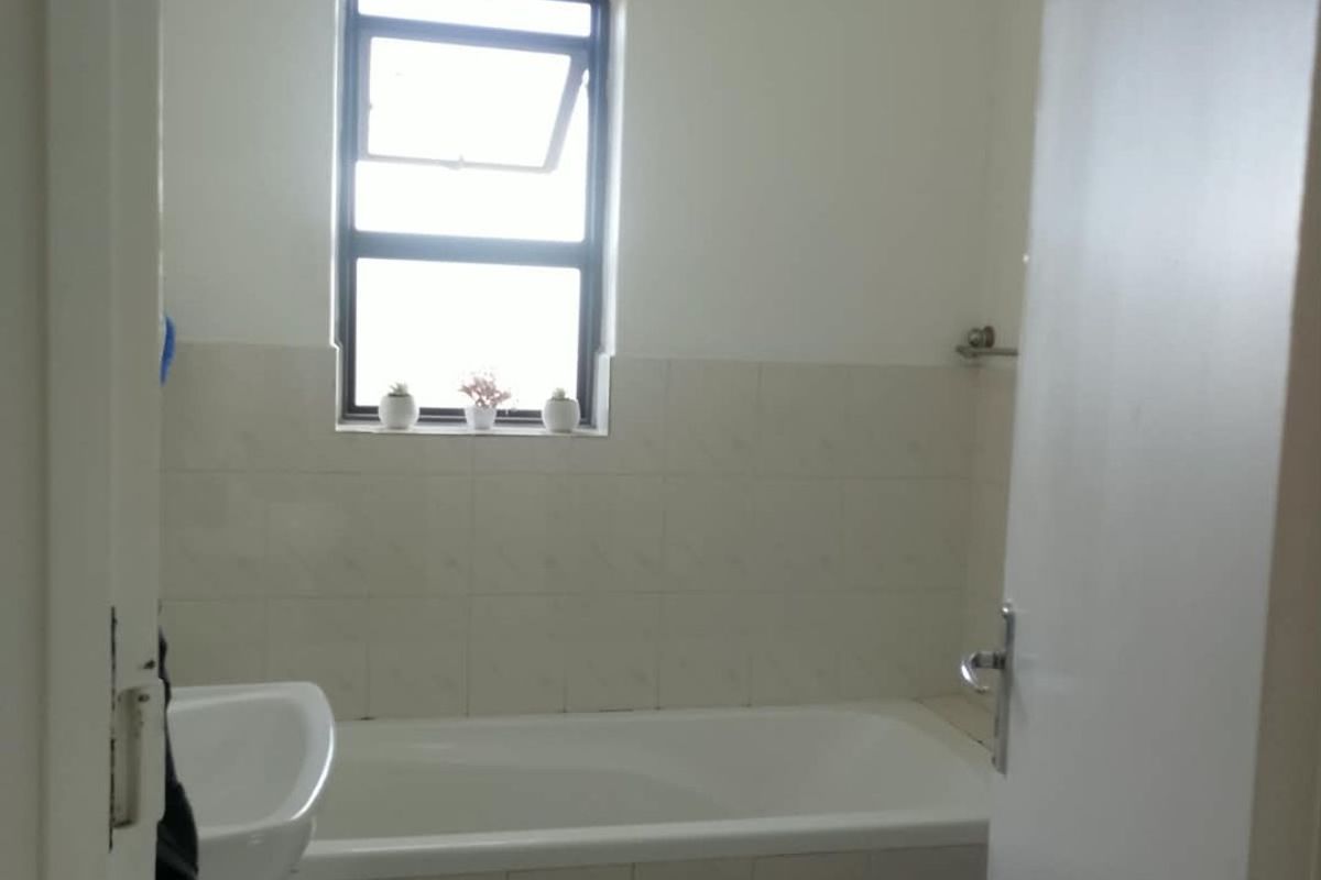 A functional bathroom featuring a bathtub, pedestal basin, and toilet with neutral wall and floor tiling.