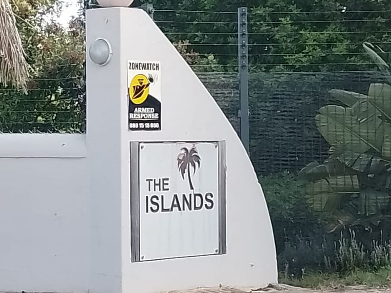 Entrance signage and boundary wall for The Islands residential complex, featuring perimeter security fencing and paved driveway access.