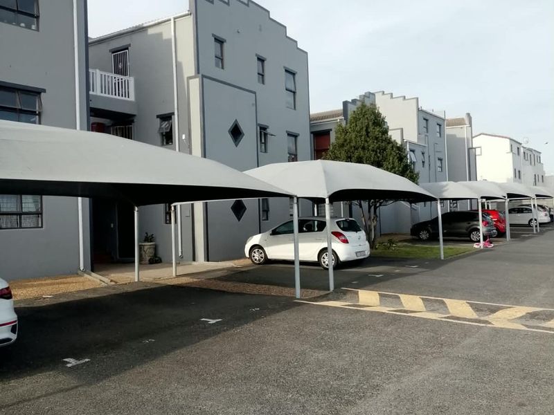 Exterior view of a multi-story apartment complex featuring covered parking bays and paved driveway access.