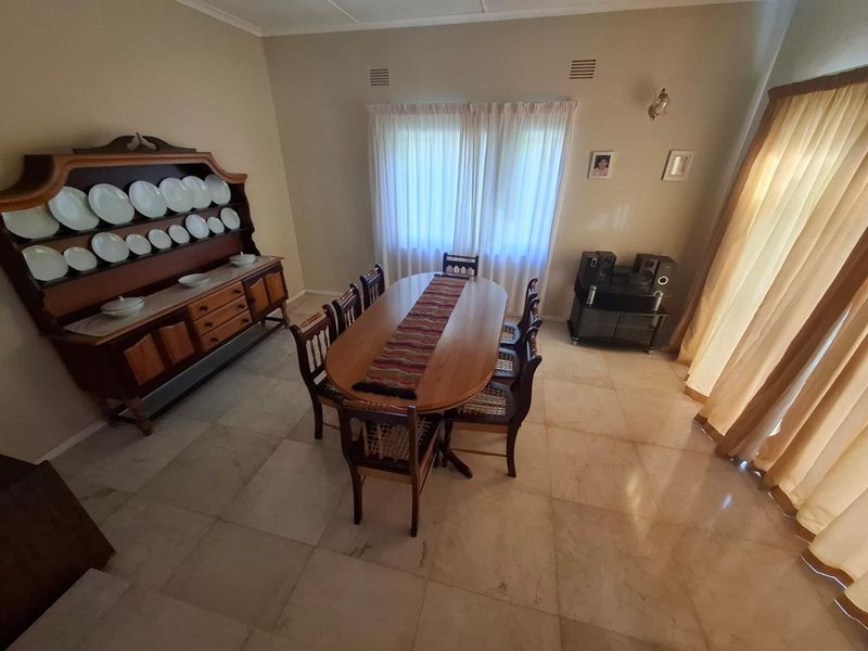 A dining room featuring large format floor tiles, neutral wall paint, and natural light through window curtains.