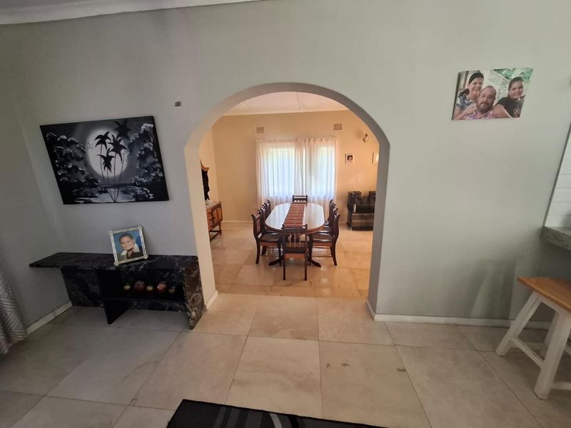 A dining room area viewed through an arched doorway, featuring tiled flooring and natural light from the window.