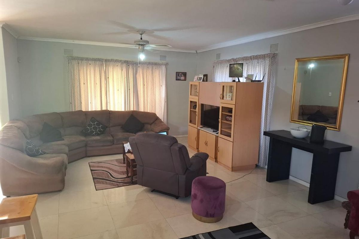 Spacious living room featuring neutral tiled flooring, ceiling fan, and large windows with curtain rails, offering a comfortable and functional family space.