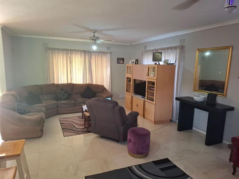 Spacious living room featuring neutral tiled flooring, ceiling fan, and large windows with curtain rails, offering a comfortable and functional family space.
