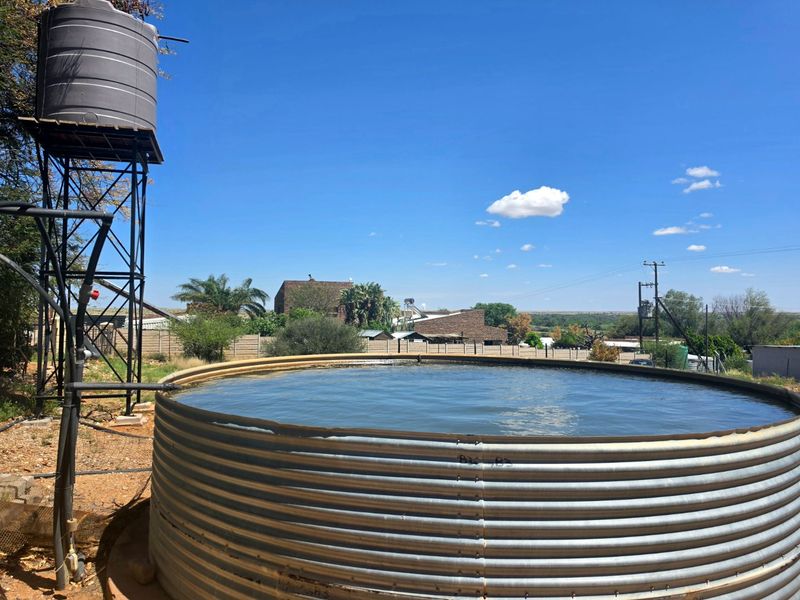 Outdoor area featuring a large corrugated steel water reservoir and an elevated plastic water storage tank with supporting steel structure.