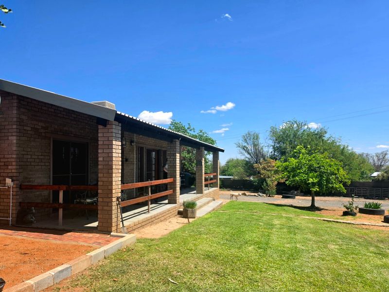 A rear view of the house featuring a covered brick patio with timber railings, overlooking a well-maintained lawn and garden area.