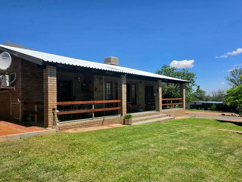 A rear view of a brick house featuring a covered patio with timber railings, a corrugated metal roof, and an installed evaporative cooling unit.