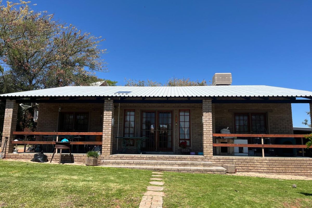 Rear view of a single-story brick house featuring a covered patio with timber railings, a corrugated metal roof, and a landscaped garden path.