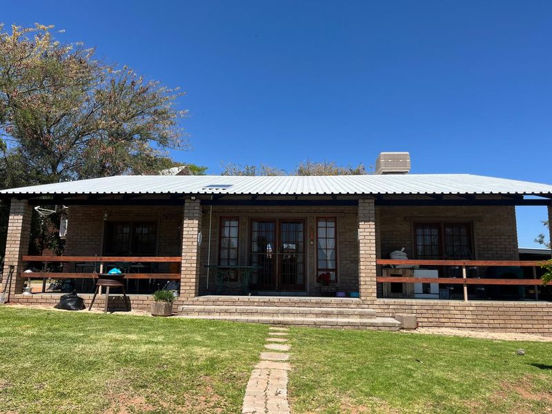 Rear view of a single-story brick house featuring a covered patio with timber railings, a corrugated metal roof, and a landscaped garden path.