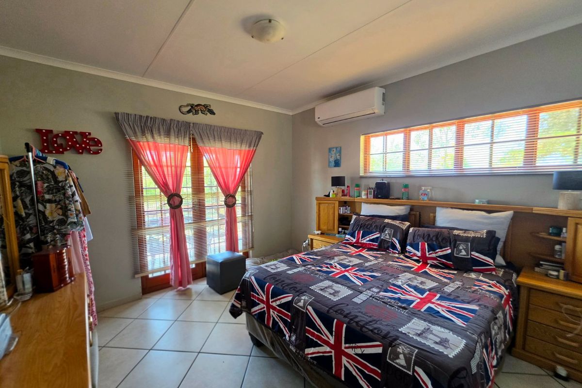 A bedroom featuring tiled flooring, a built-in headboard, and a wall-mounted split-system air conditioner with access to the outdoors via french doors.