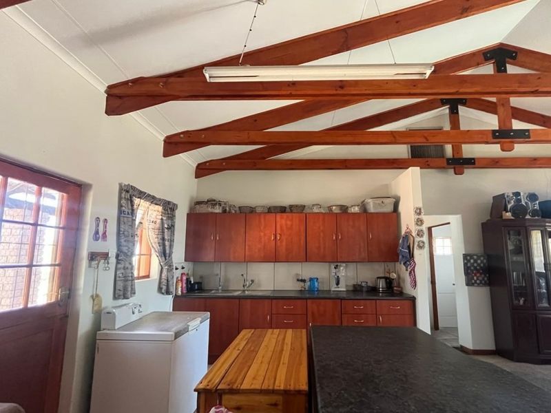 A rustic kitchen featuring exposed timber roof trusses, built-in wooden cabinetry, and a tiled backsplash, offering a functional layout with potential for modernization.
