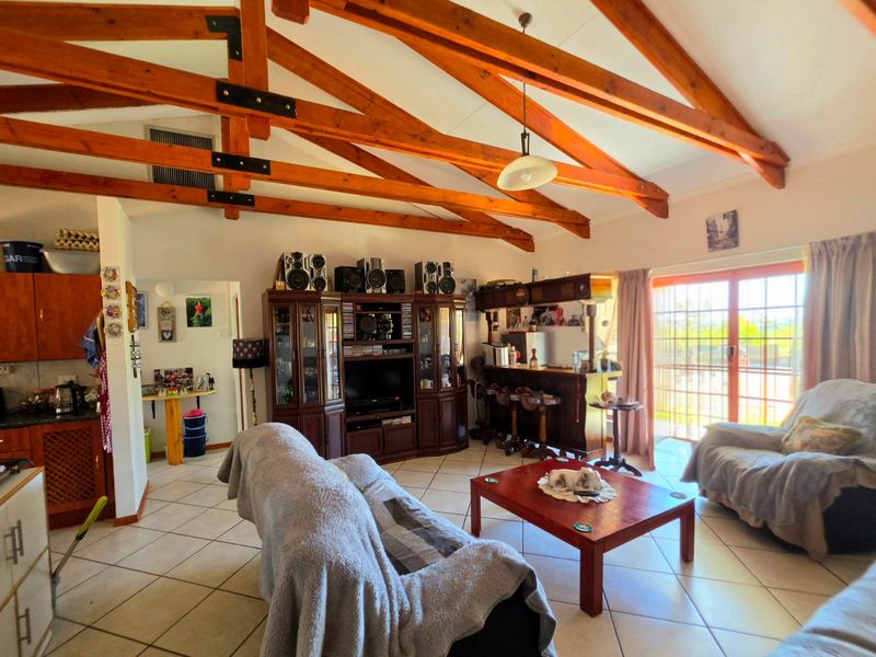 Spacious open-plan living area featuring exposed timber roof trusses, ceramic tiled flooring, and a built-in bar, with direct access to the patio.