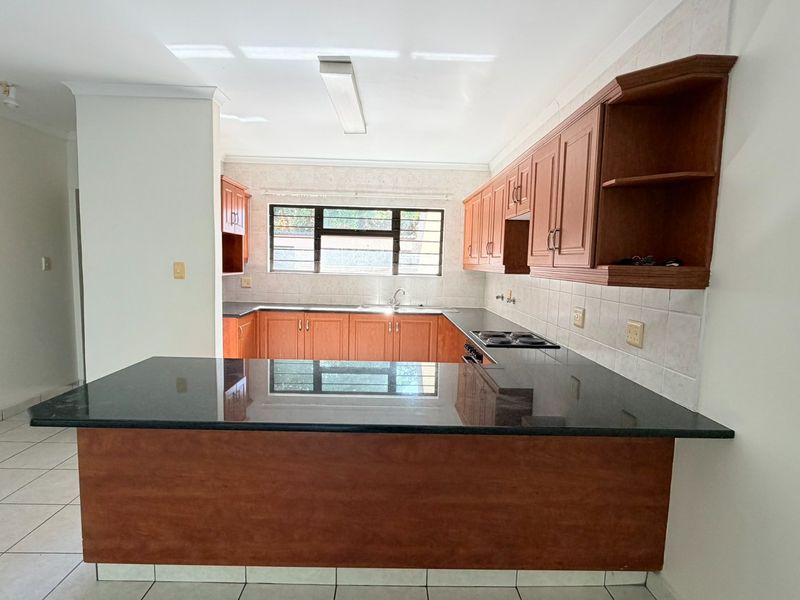 A functional kitchen featuring wooden cabinetry, granite countertops, a breakfast bar, and an integrated electric hob, offering a clean and practical workspace.