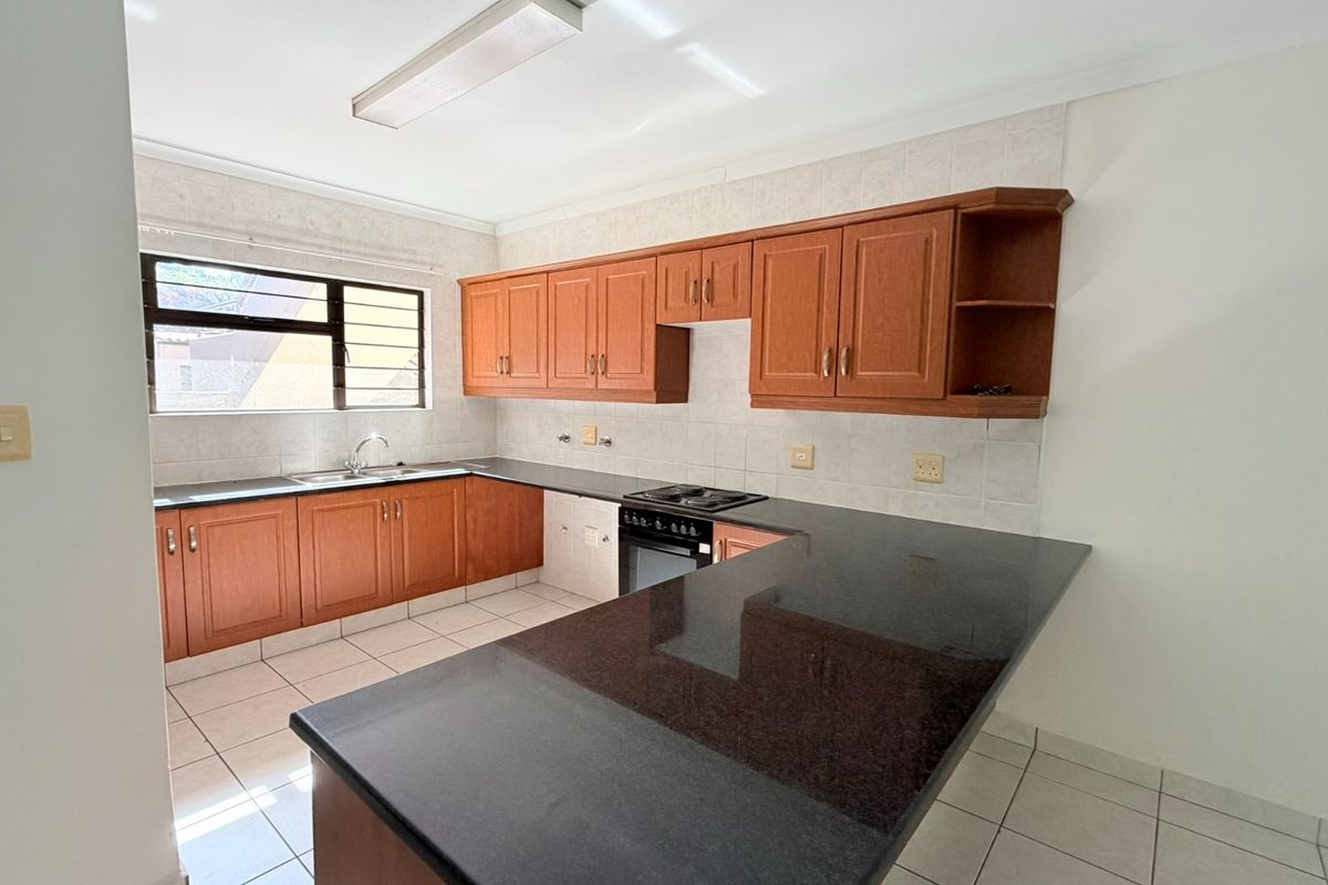 A functional kitchen featuring wooden cabinetry, granite countertops, a built-in oven and hob, and tiled flooring in a clean, empty space.