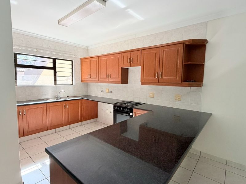 A functional kitchen featuring wooden cabinetry, granite countertops, a built-in oven and hob, and tiled flooring in a clean, empty space.