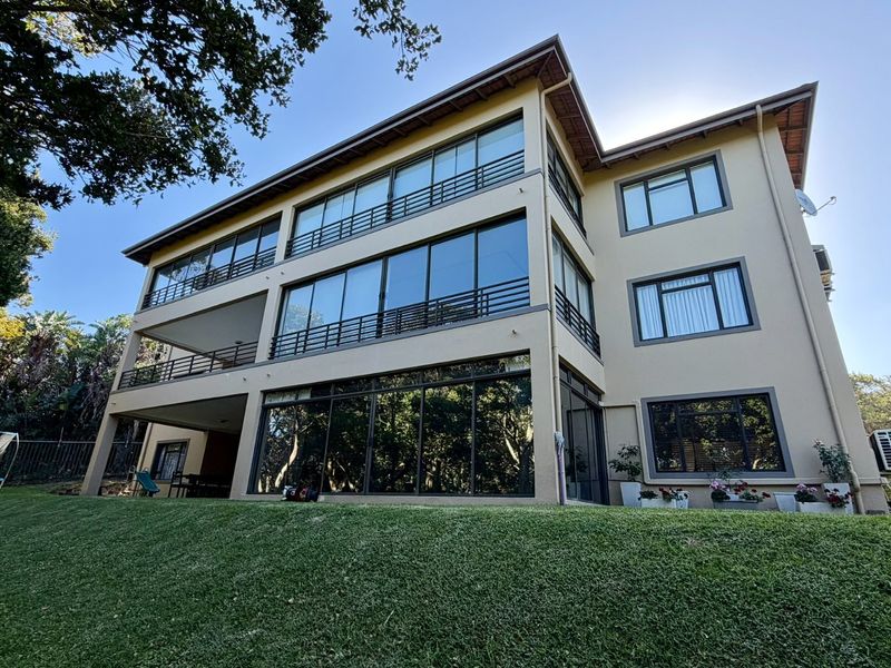 Rear view of a multi-story apartment building featuring expansive glass sliding doors, private balconies with metal railings, and a well-maintained lawn.