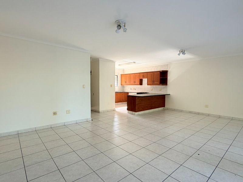 Spacious open-plan living and kitchen area featuring tiled flooring, wooden cabinetry, and a functional kitchen island layout.