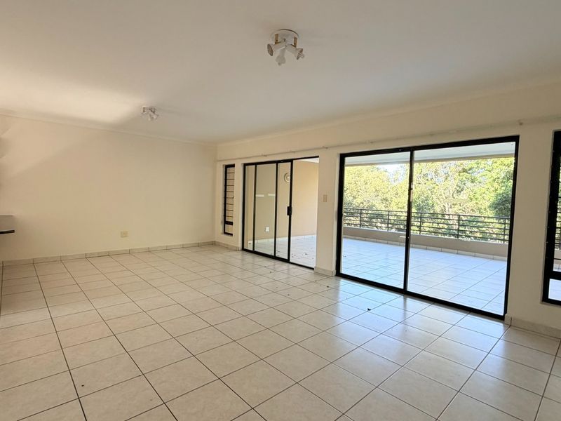 Spacious open-plan living area featuring tiled floors, kitchen cabinetry, and large sliding glass doors leading to a private balcony with scenic views.
