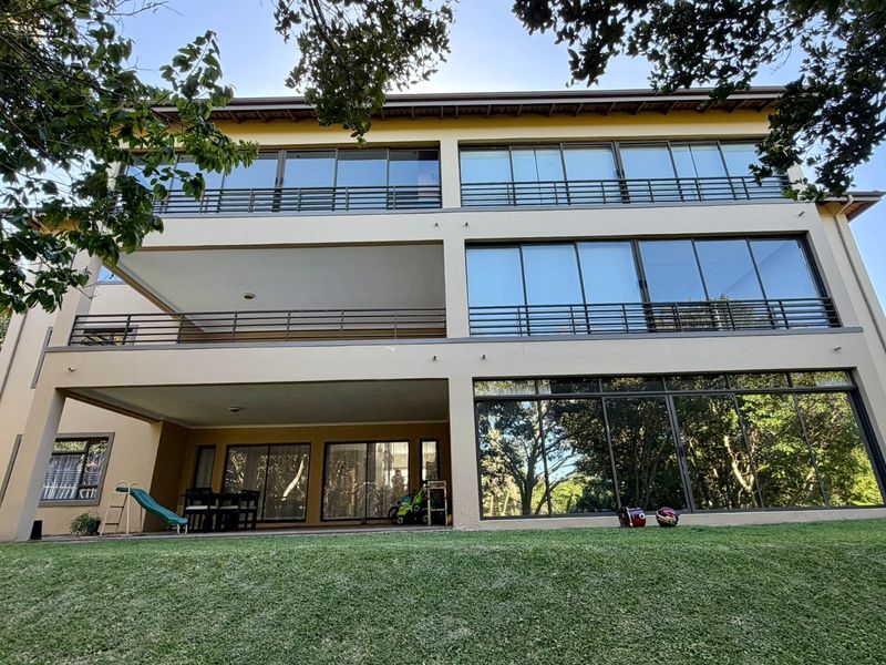 Rear elevation of a multi-story apartment building featuring expansive sliding glass doors, private balconies with metal railings, and a well-maintained lawn.