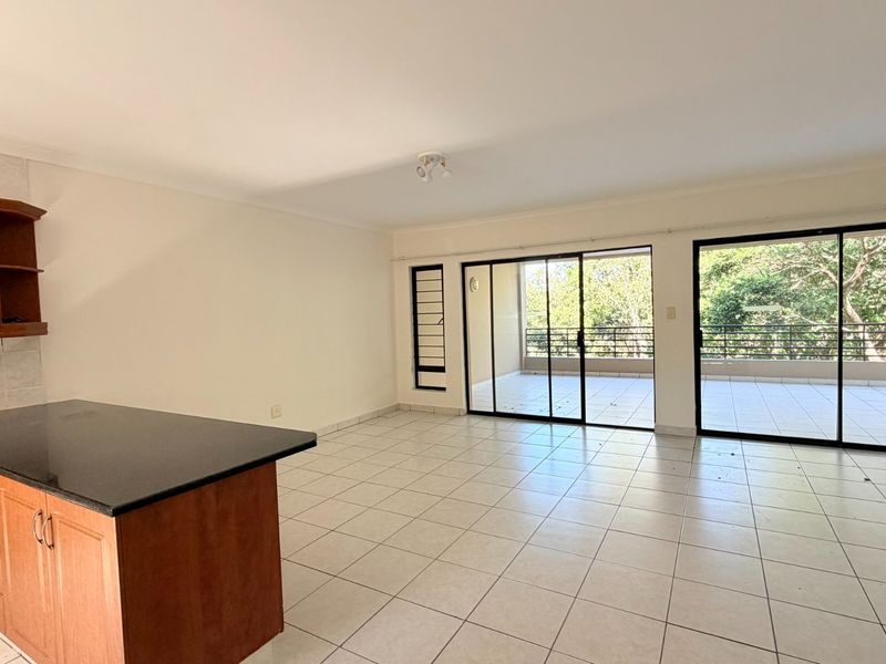 Spacious open-plan living area featuring tiled floors, kitchen cabinetry with granite countertops, and large sliding doors leading to a covered balcony.